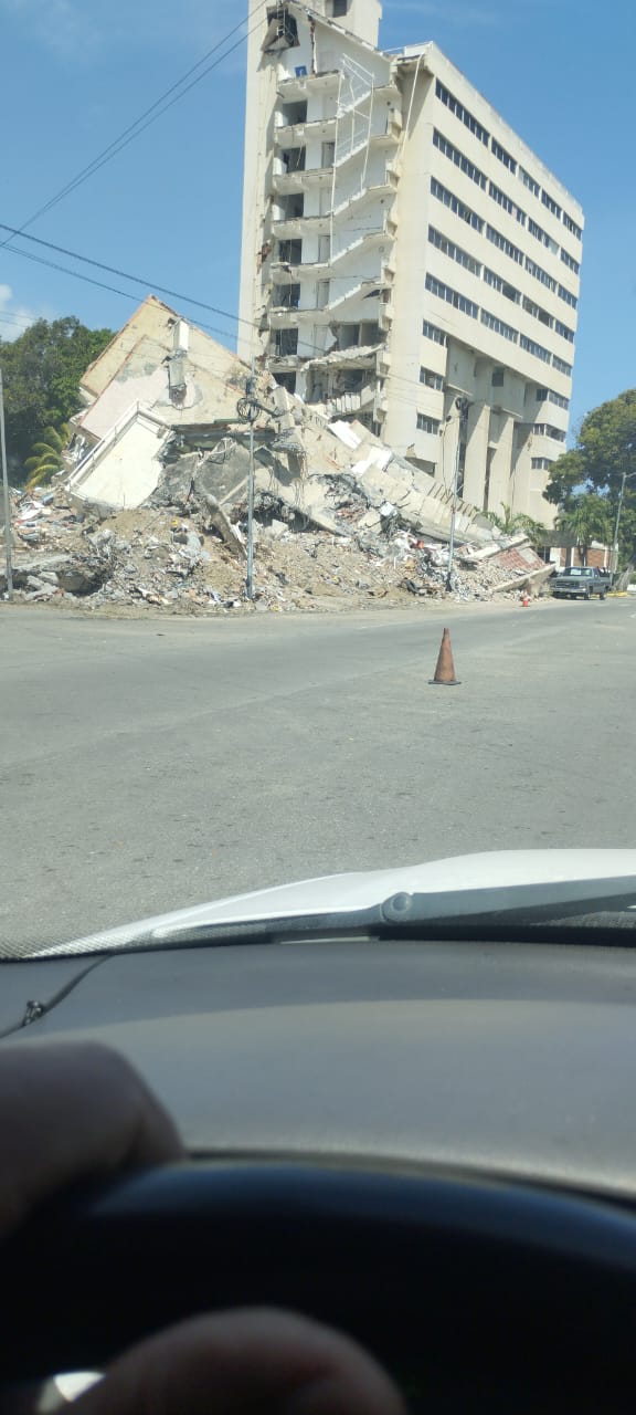 A large building with a collapsed lower structure and a wide field of rubble.