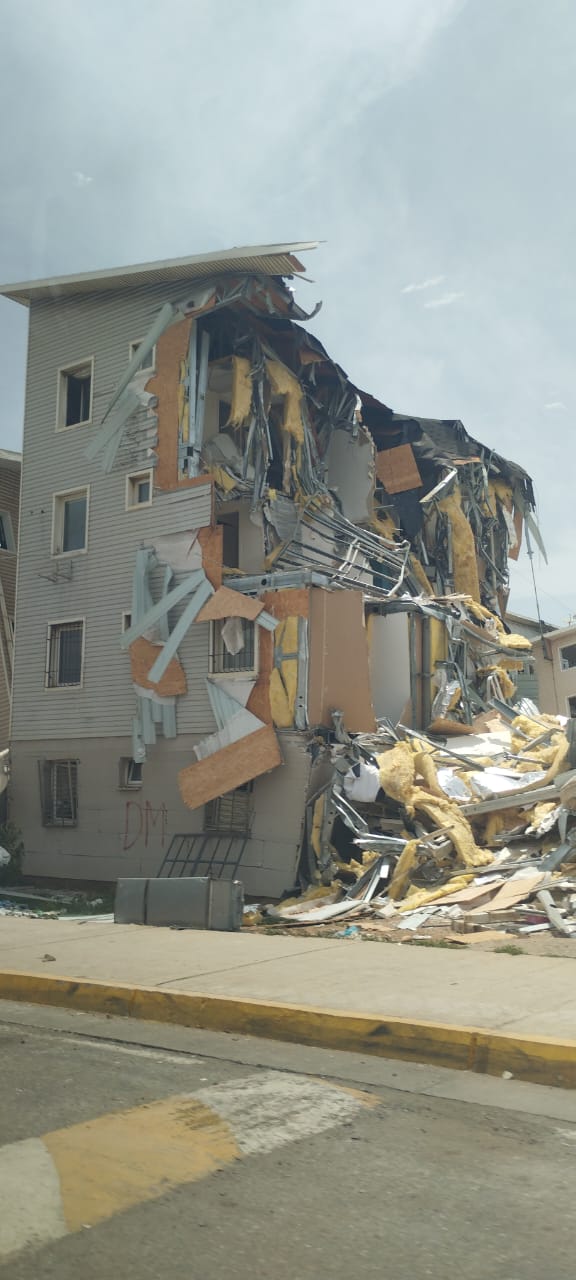 A residential building with one side collapsed, exposing damaged rooms and structural debris.